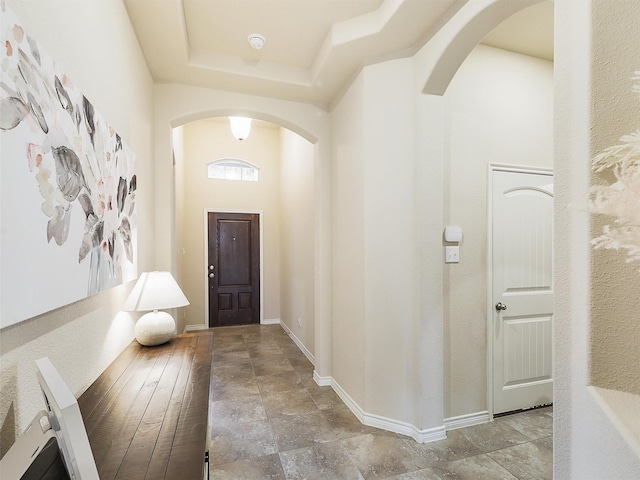 foyer featuring a raised ceiling, stone finish floor, arched walkways, a high ceiling, and baseboards