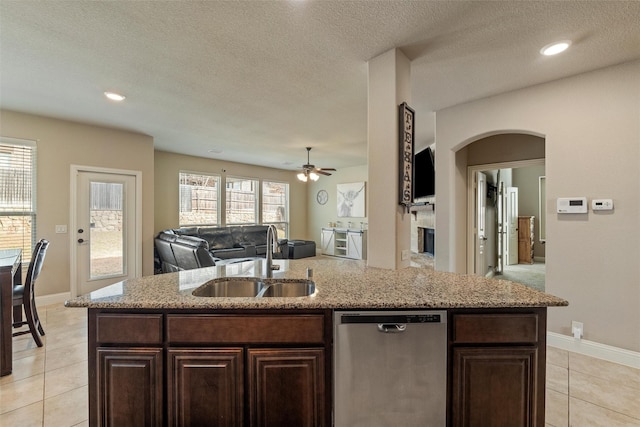 kitchen with an island with sink, light tile patterned flooring, arched walkways, a sink, and stainless steel dishwasher