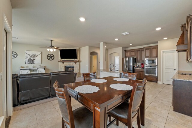 dining space featuring light tile patterned flooring, arched walkways, ceiling fan, and a fireplace