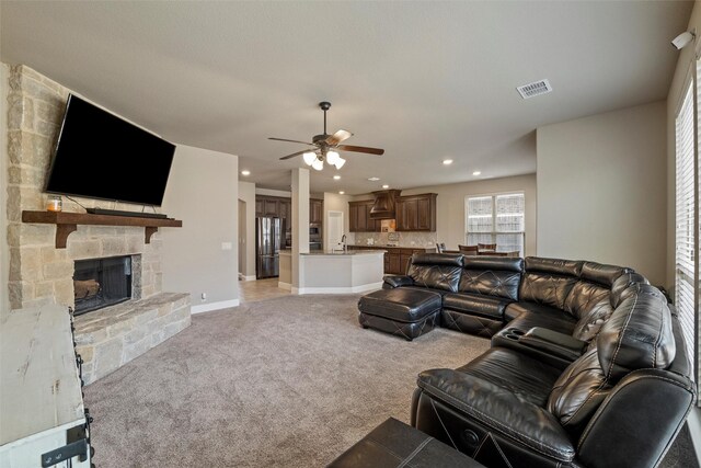 living room with visible vents, a stone fireplace, baseboards, light colored carpet, and ceiling fan