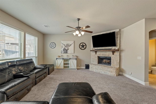 living area featuring a ceiling fan, visible vents, carpet floors, arched walkways, and a stone fireplace