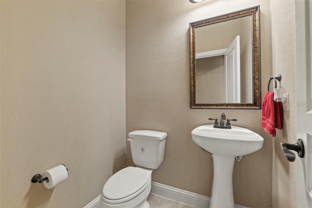 half bath featuring toilet, baseboards, and a sink