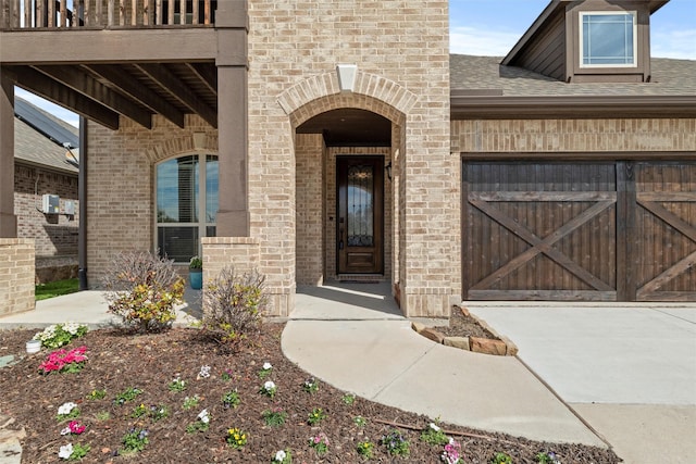 view of exterior entry with brick siding, roof with shingles, and a balcony