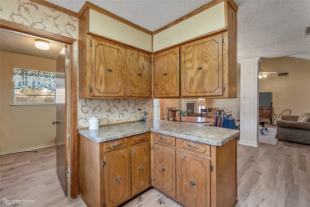 kitchen featuring brown cabinets, light wood-style floors, a peninsula, and a textured ceiling