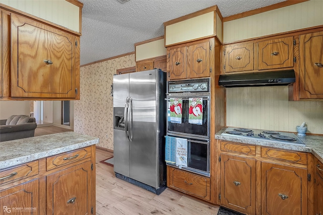 kitchen featuring a textured ceiling, wallpapered walls, ornamental molding, under cabinet range hood, and appliances with stainless steel finishes