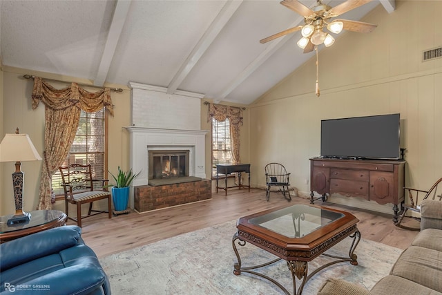 living area featuring beamed ceiling, visible vents, wood finished floors, a fireplace, and ceiling fan