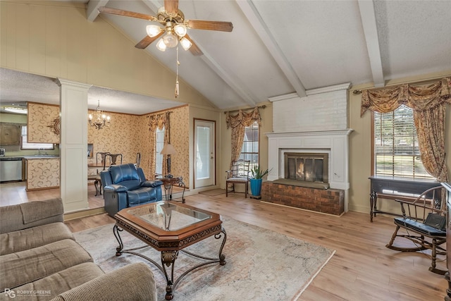 living area featuring a fireplace, ceiling fan with notable chandelier, light wood-style floors, and a textured ceiling