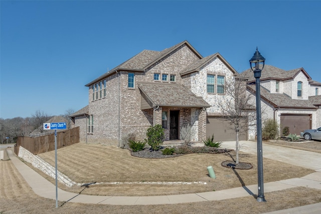 french country home featuring fence, roof with shingles, concrete driveway, a garage, and brick siding