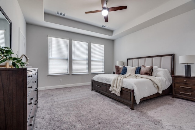 bedroom featuring visible vents, light colored carpet, a tray ceiling, and baseboards