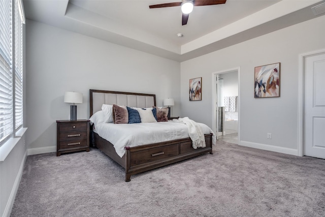 carpeted bedroom with baseboards, a raised ceiling, ceiling fan, and ensuite bathroom