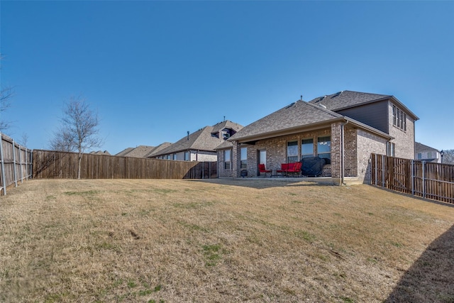 rear view of property with a lawn, brick siding, a fenced backyard, and a shingled roof