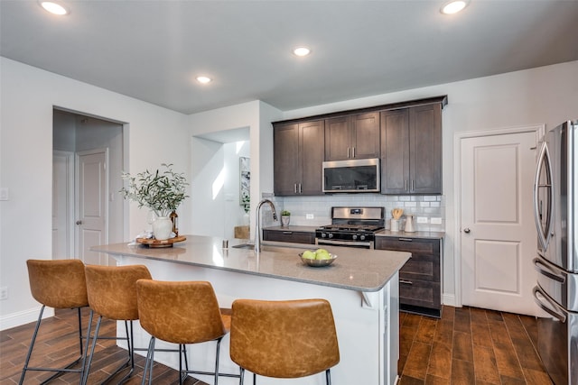 kitchen with decorative backsplash, dark wood-type flooring, dark brown cabinets, and appliances with stainless steel finishes