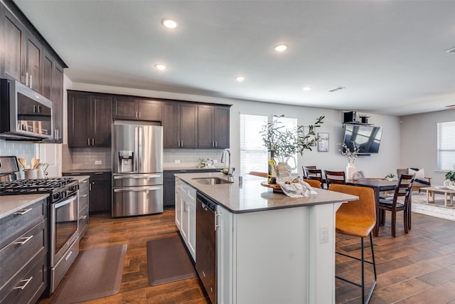 kitchen featuring a sink, a kitchen bar, a wealth of natural light, appliances with stainless steel finishes, and dark wood-style flooring