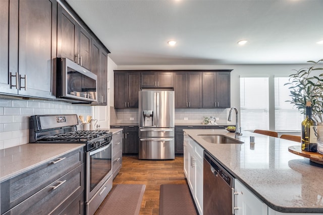 kitchen with dark brown cabinets, dark wood-type flooring, light stone counters, appliances with stainless steel finishes, and a sink