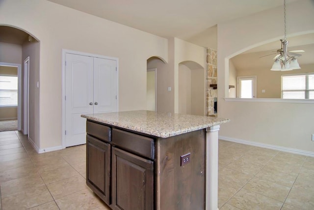 kitchen featuring light stone counters, a kitchen island, dark brown cabinetry, baseboards, and ceiling fan