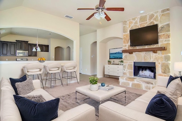 living area with visible vents, a stone fireplace, light colored carpet, ceiling fan, and vaulted ceiling