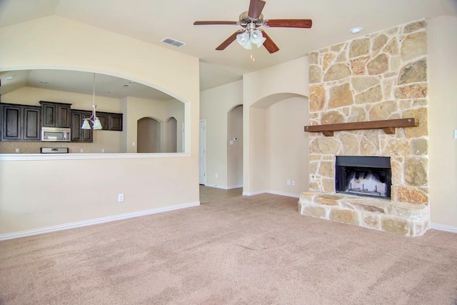 unfurnished living room with visible vents, carpet, ceiling fan, vaulted ceiling, and a stone fireplace