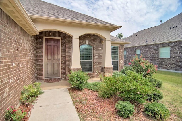 property entrance with a yard, brick siding, and a shingled roof