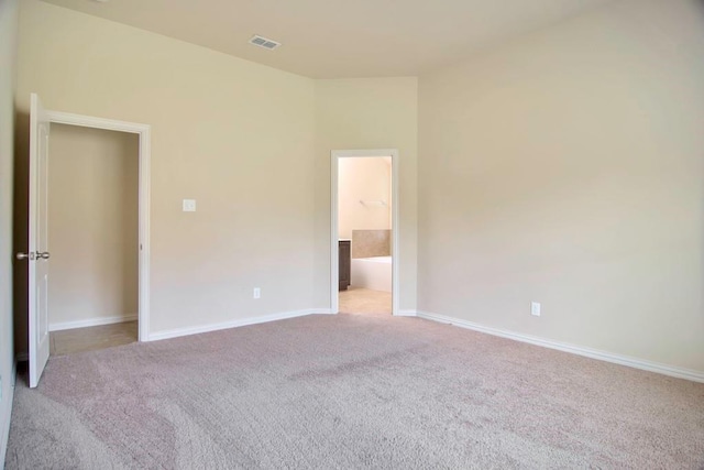 unfurnished bedroom with visible vents, baseboards, light colored carpet, and ensuite bathroom