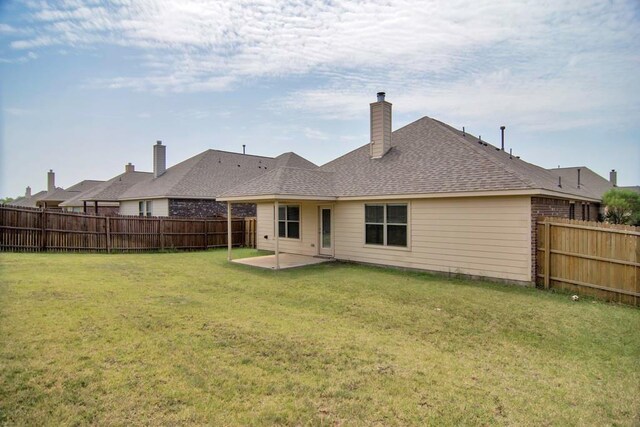 back of property with a fenced backyard, a yard, roof with shingles, a chimney, and a patio area