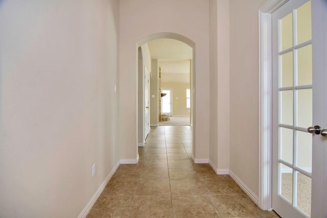 hall featuring arched walkways, light tile patterned floors, and baseboards