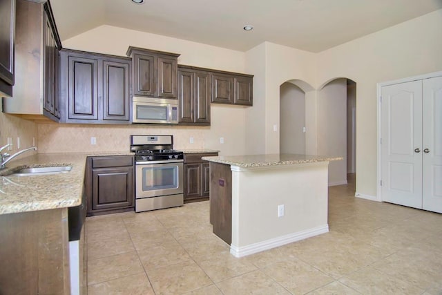 kitchen with light stone counters, a sink, dark brown cabinets, appliances with stainless steel finishes, and a center island