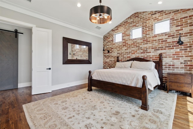 bedroom with a barn door, lofted ceiling, wood finished floors, and brick wall