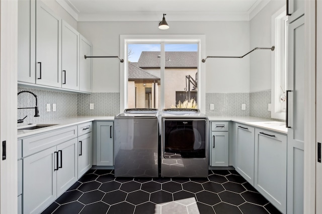 laundry room featuring washing machine and clothes dryer, cabinet space, ornamental molding, and a sink