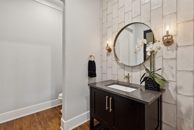 bathroom featuring baseboards, toilet, wood finished floors, and vanity