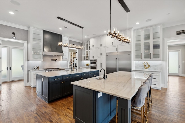 kitchen featuring a spacious island, white cabinets, stainless steel appliances, wall chimney exhaust hood, and a sink