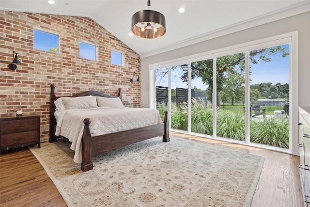 unfurnished bedroom featuring multiple windows, wood finished floors, brick wall, and vaulted ceiling