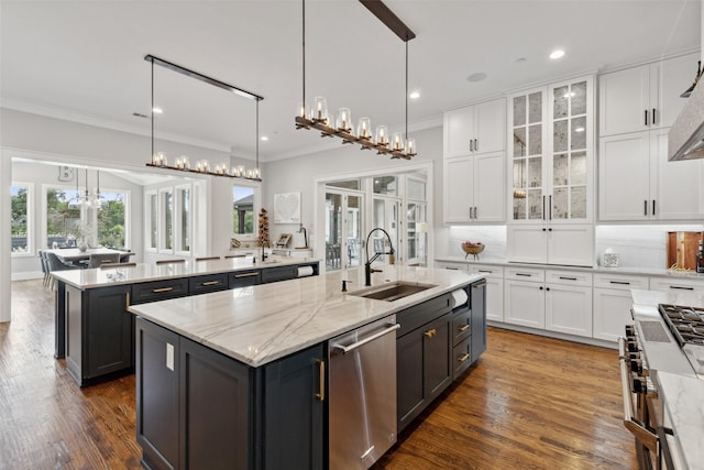 kitchen with a kitchen island with sink, a sink, hanging light fixtures, stainless steel appliances, and white cabinetry