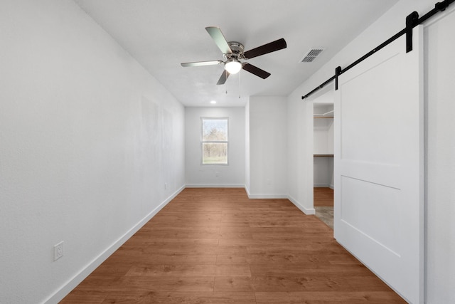 unfurnished bedroom with baseboards, visible vents, light wood finished floors, a spacious closet, and a barn door