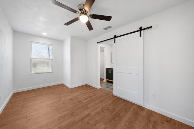 unfurnished bedroom with light wood finished floors, visible vents, baseboards, and a barn door