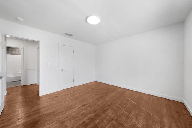 empty room featuring attic access, wood finished floors, visible vents, and baseboards