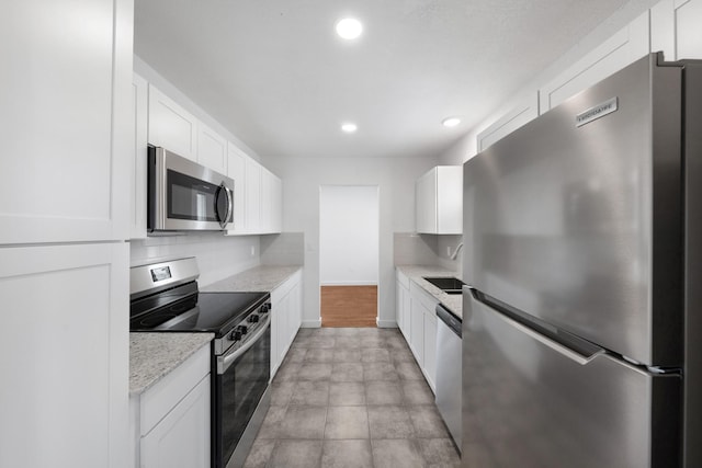 kitchen with baseboards, recessed lighting, stainless steel appliances, white cabinetry, and backsplash