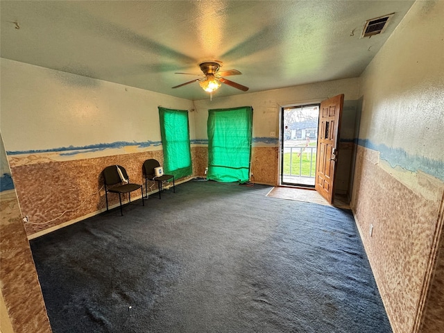 unfurnished room featuring visible vents, a wainscoted wall, a ceiling fan, a textured ceiling, and carpet