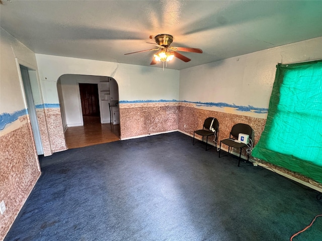 interior space with a wainscoted wall, a ceiling fan, and arched walkways