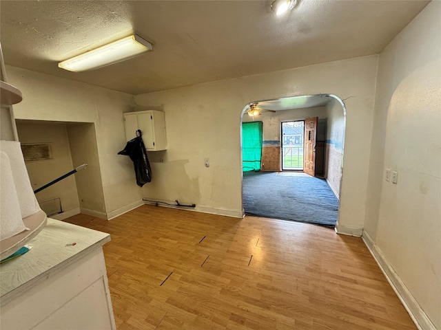 interior space with a textured ceiling, baseboards, light wood-type flooring, and ceiling fan