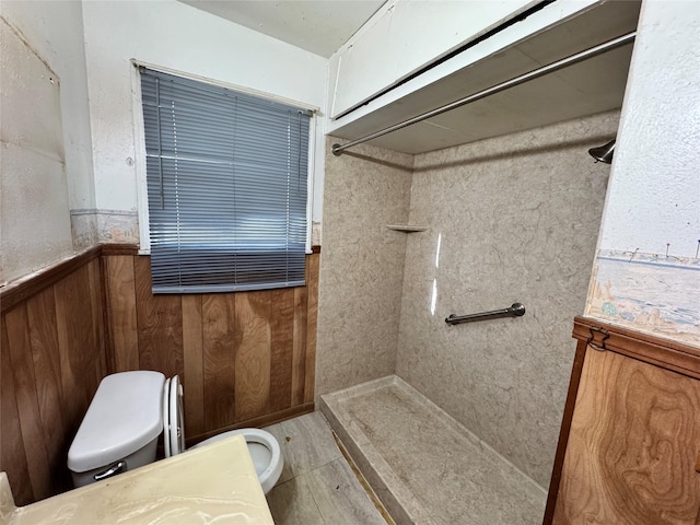 bathroom with vanity, a wainscoted wall, a tile shower, wood walls, and toilet