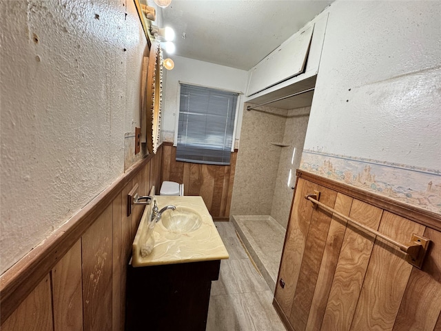 bathroom with wooden walls, wainscoting, vanity, and walk in shower