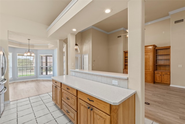 kitchen with visible vents, crown molding, light countertops, a tray ceiling, and light wood-style flooring