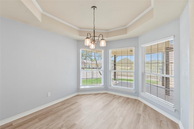 empty room featuring light wood-style flooring, ornamental molding, a tray ceiling, baseboards, and a chandelier