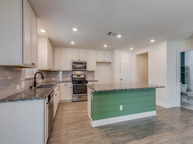 kitchen with a sink, white cabinetry, stainless steel appliances, dark stone counters, and light wood-style floors