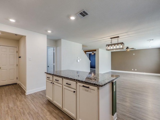 kitchen featuring light wood finished floors, visible vents, a center island, baseboards, and dark stone counters