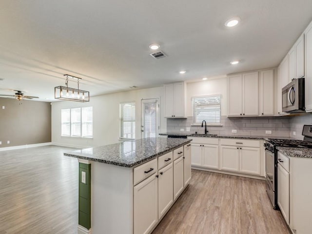 kitchen with visible vents, appliances with stainless steel finishes, white cabinets, light wood finished floors, and decorative backsplash