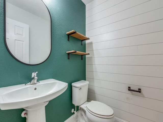 half bathroom with toilet, baseboards, and a sink