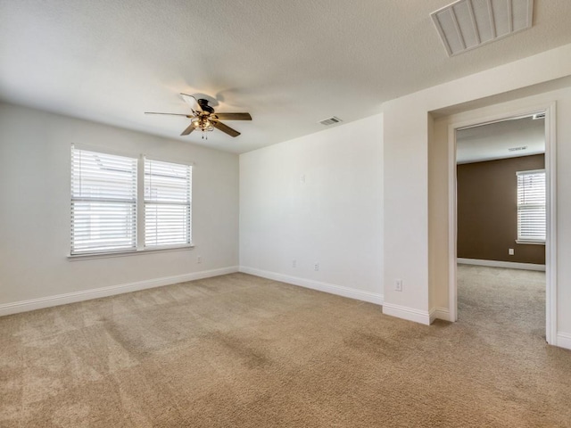 unfurnished room with light carpet, visible vents, baseboards, and a ceiling fan