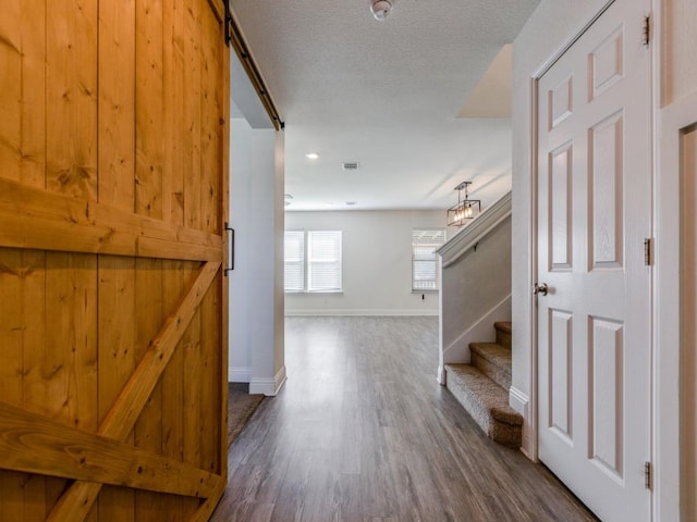 hall featuring baseboards, dark wood finished floors, stairway, a barn door, and a textured ceiling