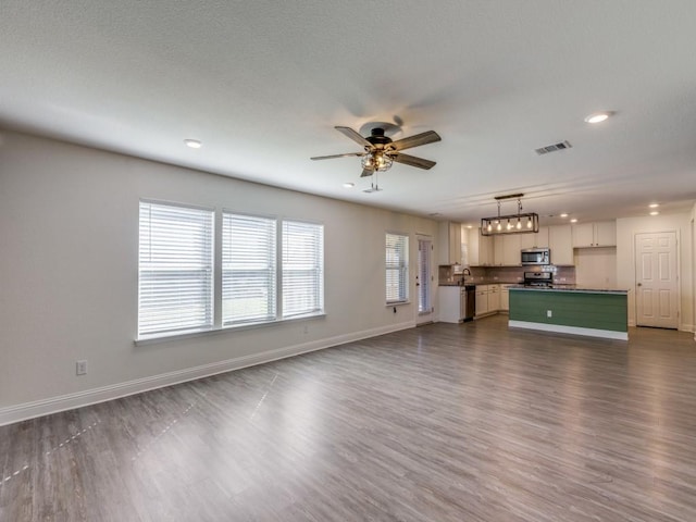 unfurnished living room featuring a ceiling fan, dark wood-style floors, visible vents, and baseboards